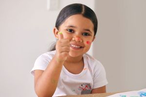 Smiling child holding thumbs up while fingerpainting